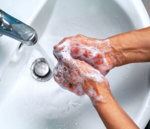 Hands being washed under running water in a white basin to promote hygeine.