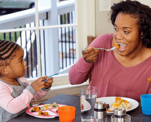 Small girl having dinner with her mom, both glancing at each other happily.